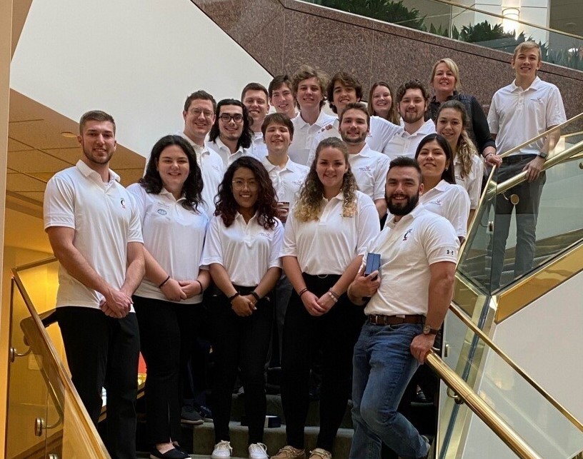 group of a dozen college students in white polo shirts pose on stairs