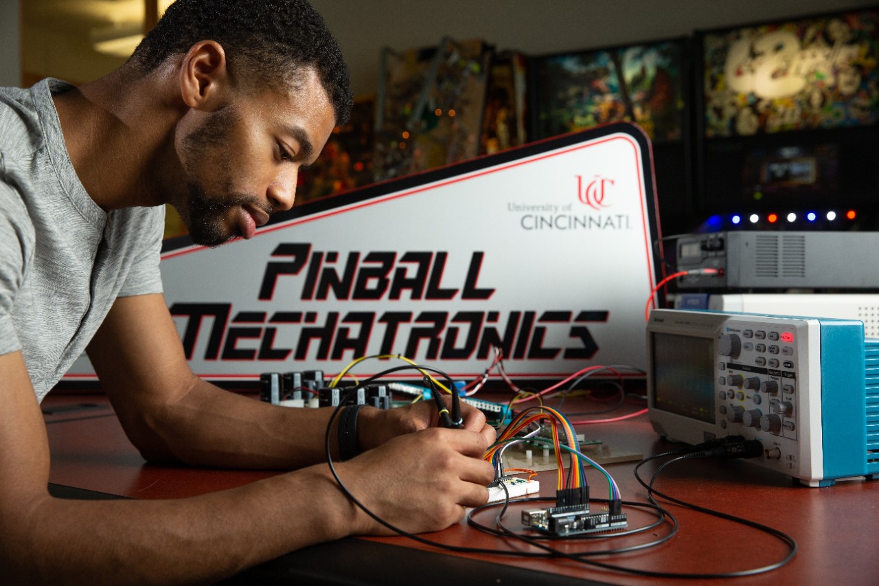 Students pose in CEAS Professor Zach Fuchs's lab, where he uses pinball mechatronics to demonstrate principles of electrical engineering.