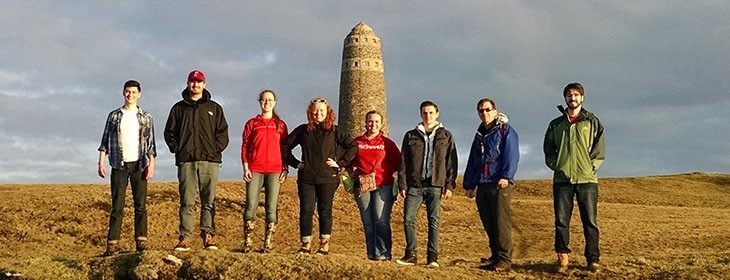 Group of 8 students standing on a mountain with a monument in the background