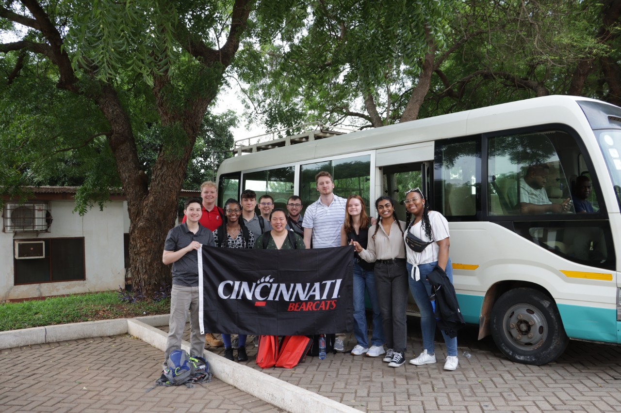 Students arriving in Ghana stand in front of bus holding UC banner