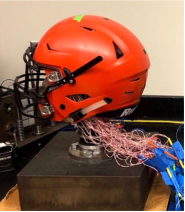 A red sports helmet sits on a pedestal for testing. 