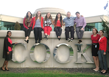 Costina Luc, biomedical engineering class of 2018, is sitting on top of the large "Cook" company sign with her coworkers