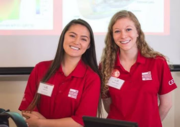 Kaitlin Stock, mechanical engineering class of 2018, is pictured here with her fellow CEAS ambassador, Costina Luc, and they are both wearing their red CEAS "We Engineer Better" polo shirts.
