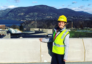 Kearstin O'Mara, construction management class of 2019, pictured in front of mountains in West Point, NY. She is wearing a neon yellow safety vest, safety glasses and a yellow hardhat.